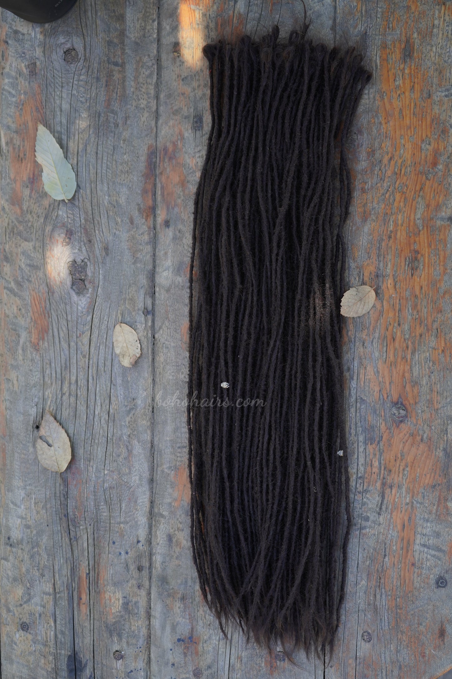 Dark brown hair extensions on a wooden surface with scattered leaves.